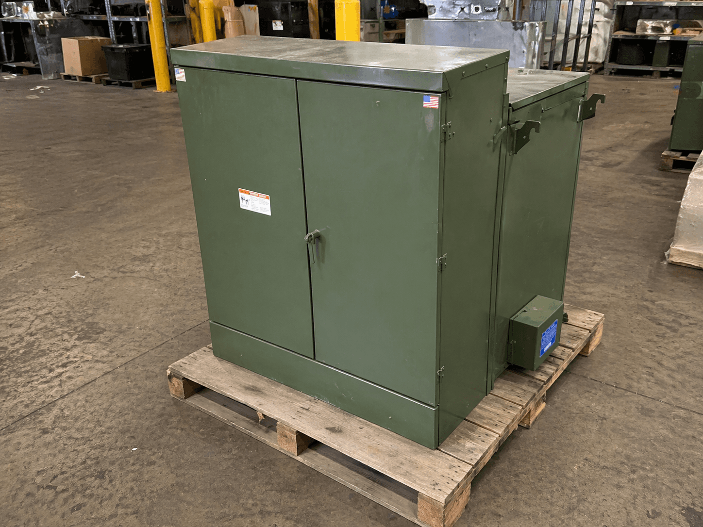 Used green industrial transformer on a pallet in a warehouse, available as balance-of-system equipment for resale